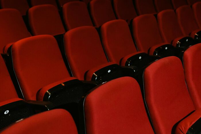 Empty red movie theater seats in a dimly lit cinema, inviting viewers to guess famous films from opening scenes.