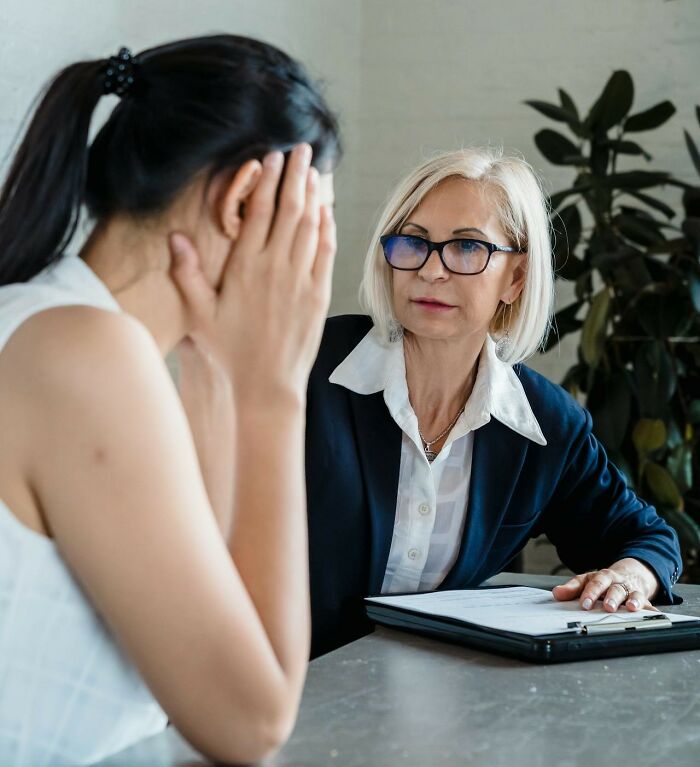 A woman consoling a distressed colleague during a serious discussion about workplace scandals in an office setting.