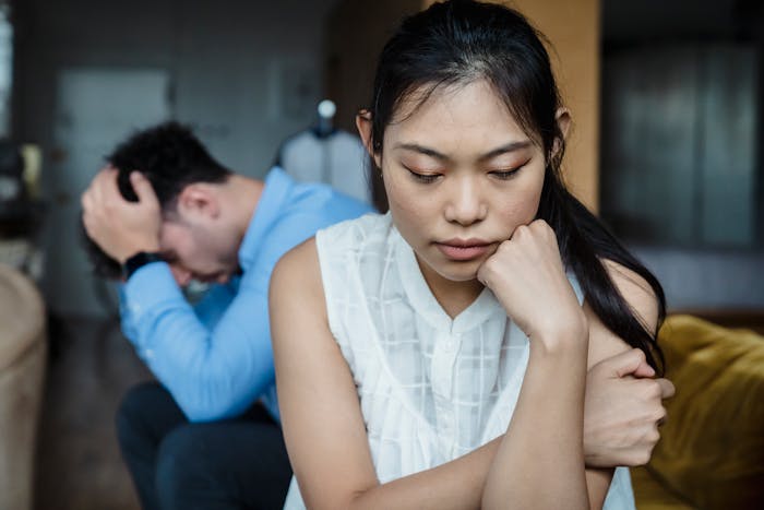 Upset woman and distressed boyfriend sitting apart inside home, showing emotional tension and conflict in relationship.