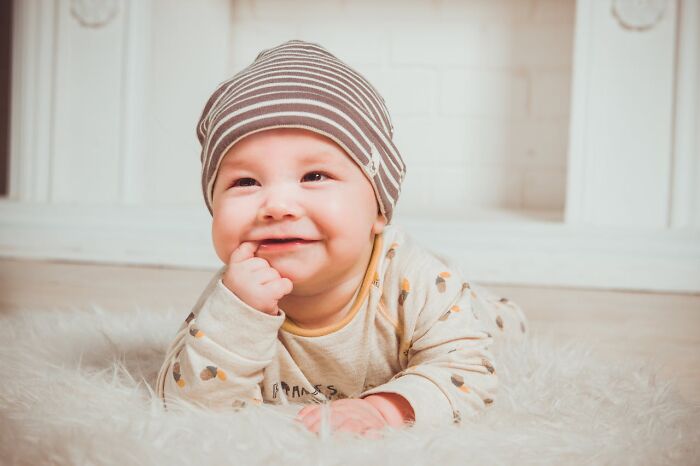 Smiling baby wearing a striped hat, lying on a fluffy surface, evoking feelings linked to unresolved mysteries and chills.