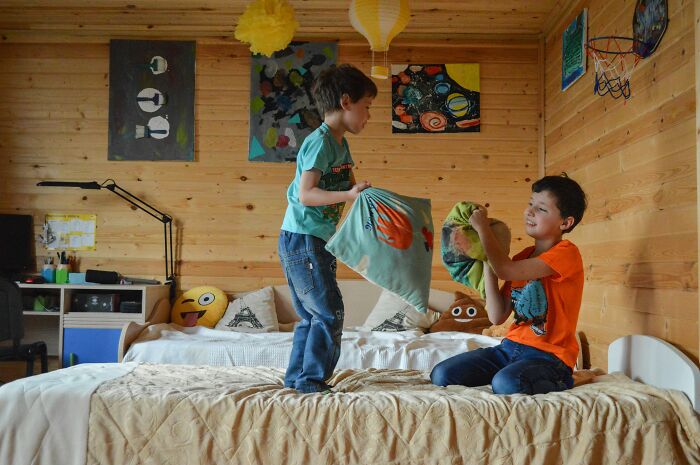 Two children having a playful pillow fight in a bedroom, capturing moments of revenge stories with a bitter aftertaste.