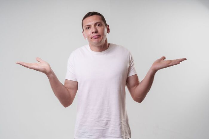 Man in a white t-shirt shrugging with both hands, expressing confusion about a glitch in the system concept.