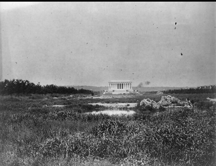 Vintage black and white historical picture showing a distant view of the Lincoln Memorial surrounded by fields and trees.