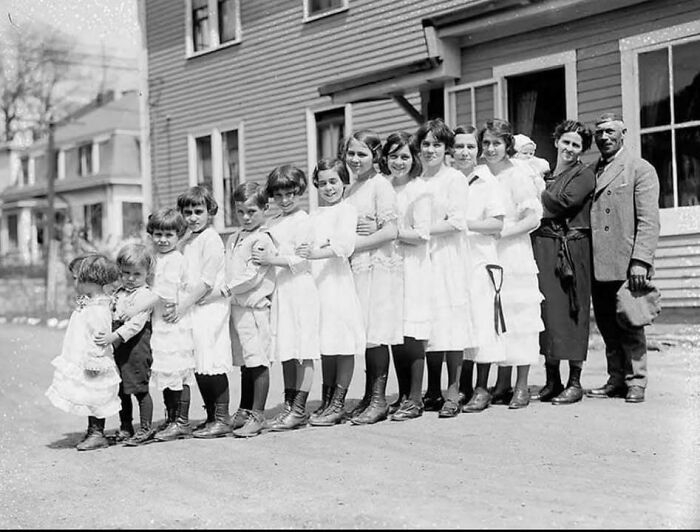 Black and white historical picture of a large family standing in a line outside classic homes on a street.
