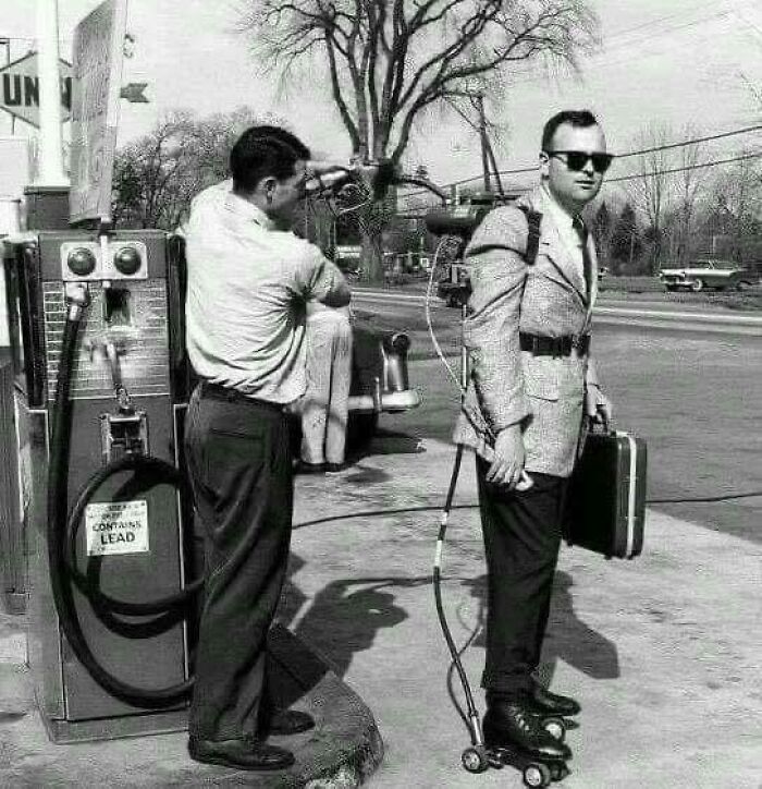 Man wearing roller skates and a fuel tank on his back getting gasoline from a gas station in a historical picture