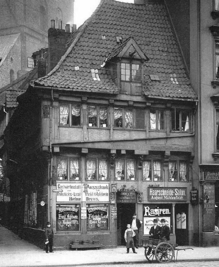 Historic black and white photo of a classic European building with people and a cart on the street outside.