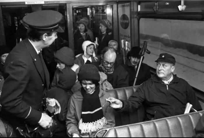 Black and white historical picture showing passengers and a conductor interacting inside a vintage bus or tram.