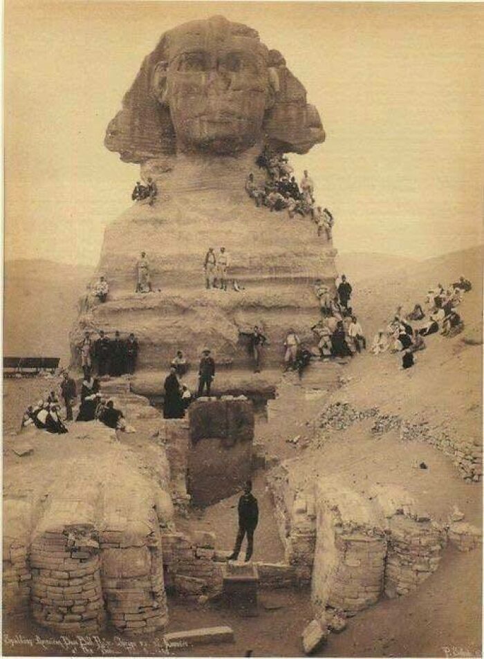 Historic sepia photo of the Great Sphinx of Giza with people gathered around the ancient monument ruins.