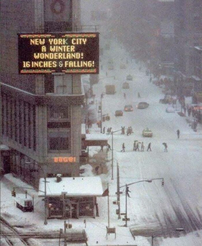 Snow-covered New York City street with people crossing and a sign announcing 16 inches of snowfall, classic historical picture.