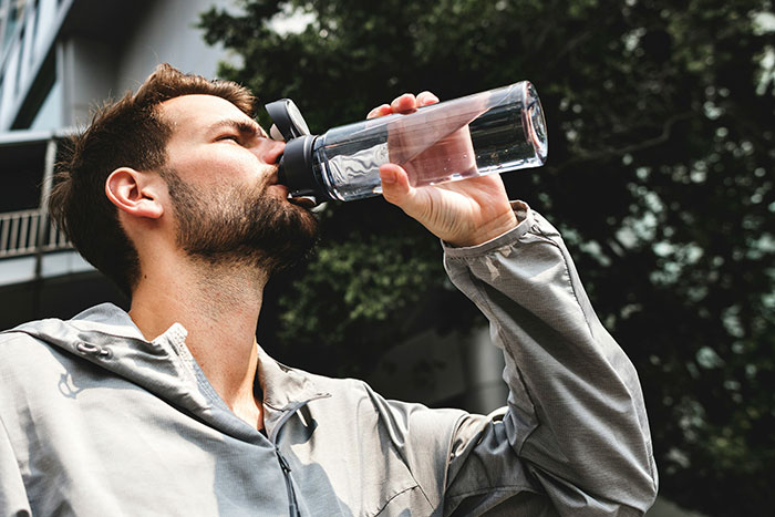 Man drinking water from reusable bottle outdoors, illustrating easy ways to save money with poor person hacks.