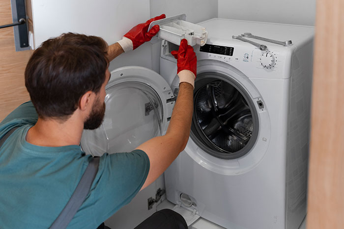 Man wearing red gloves repairing a washing machine, demonstrating poor person hacks to easily save thousands on household expenses.