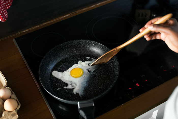 Hand stirring a single egg frying in a pan on a stovetop demonstrating easy poor person hacks to save money.