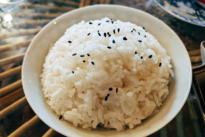 Bowl of cooked white rice topped with black sesame seeds, representing easy and affordable meal hacks to save money.
