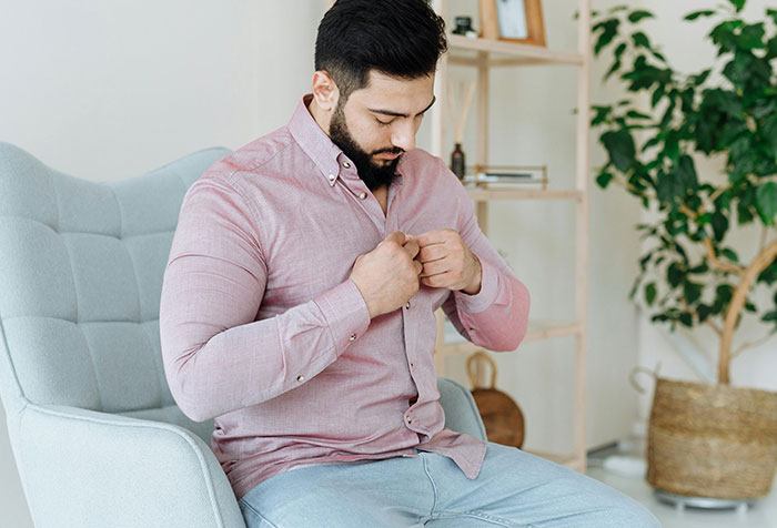 Man sitting in armchair buttoning pink shirt, symbolizing resistance to toxic masculinity and microfeminism themes.