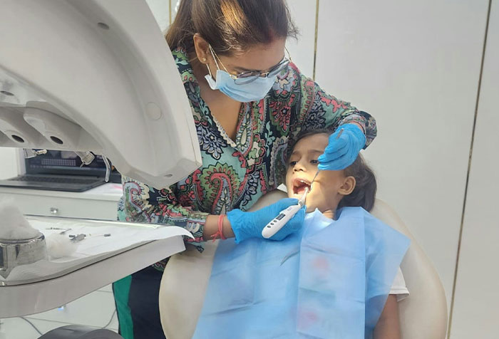 Woman wearing mask and gloves examining a child’s teeth at a dental clinic, showcasing care and professionalism.