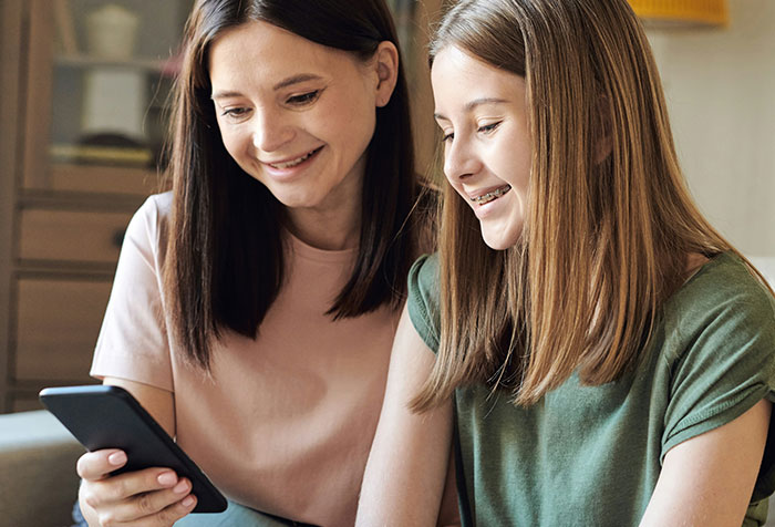 Two women smiling and looking at a phone together, representing acts of microfeminism against toxic masculinity.