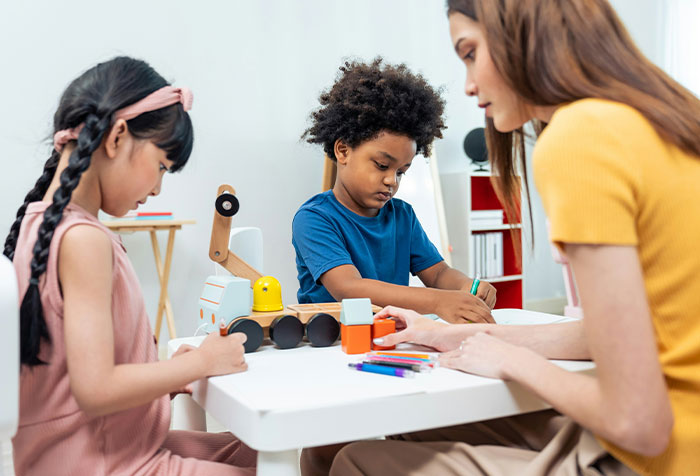 Three children drawing at a table, illustrating young girls clapping back at toxic masculinity with microfeminism acts.