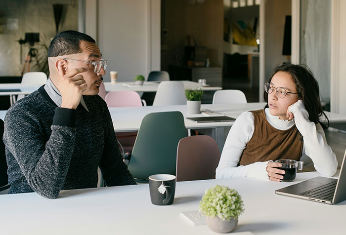 Two colleagues discussing ideas over coffee in an office, illustrating women clapping back at toxic masculinity.