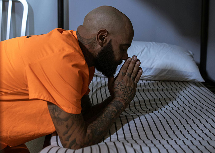 Inmate in orange prison uniform praying on bed, illustrating surprising facts and misconceptions about prison life.