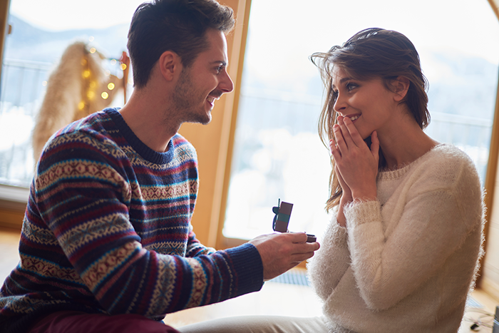 Man proposing to woman indoors with a ring, highlighting a bride&rsquo;s emotional moment before wedding vows.