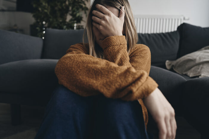Young woman sitting on floor covering her face, illustrating habits affecting mental and physical health long-term.