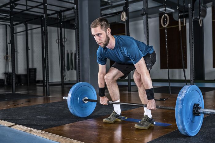 Man lifting weighted barbell in gym, demonstrating habits that impact long-term mental and physical health.