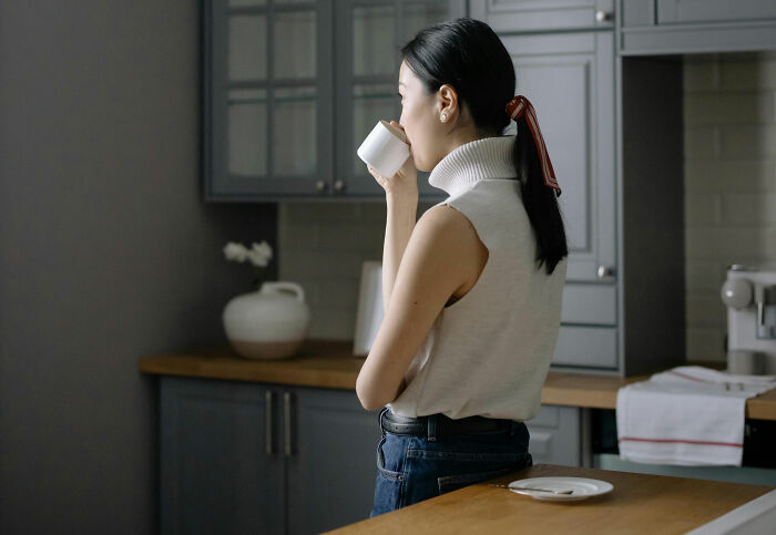 Woman drinking coffee in a modern kitchen, representing habits that affect mental and physical health long-term.
