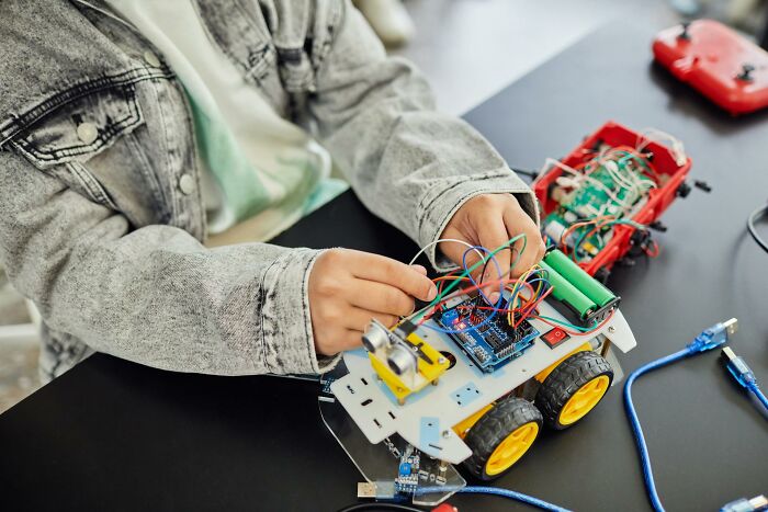 Person assembling an electronic robot vehicle with wires and circuits, illustrating creative work after quitting jobs fast.