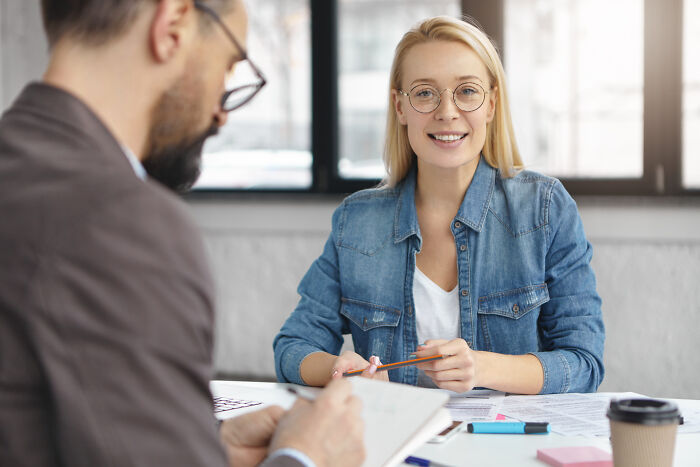 Young woman sharing wild stories of quitting jobs quickly while a man takes notes during a casual office meeting.