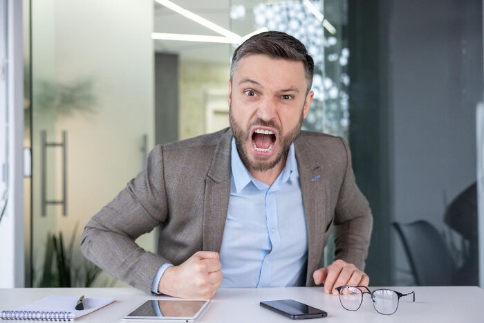 Angry man expressing frustration at office desk, illustrating wild stories of folks who quit their jobs quickly.
