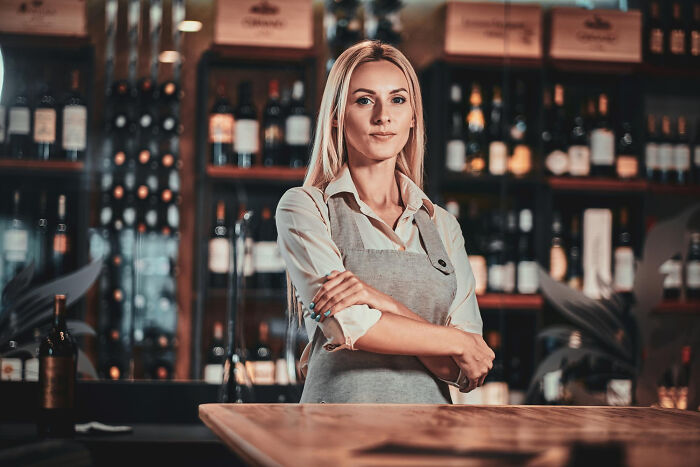 Young woman in apron standing confidently behind bar counter, representing stories of folks who quit their jobs quickly.