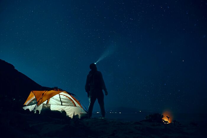 Person camping at night with tent and headlamp under starry sky, capturing moments of instinctively sensing something wrong.