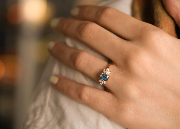 Close-up of a hand wearing a blue gemstone ring, illustrating ideas related to refuse buying engagement ring choices. Close-up of a hand wearing a blue gemstone ring, illustrating ideas related to refuse buying engagement ring choices.