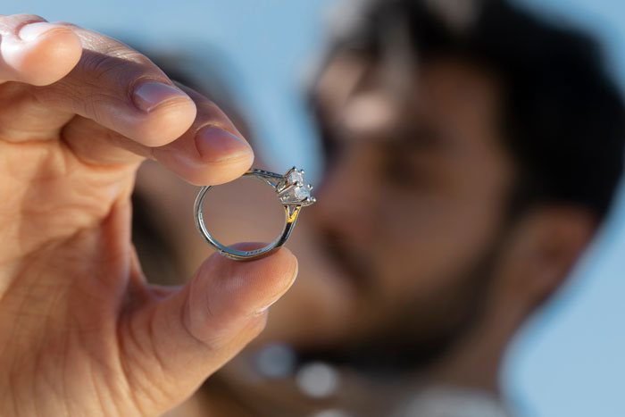 Close-up of a person holding a family heirloom ring, highlighting a diamond set in a silver band against a blurred background.