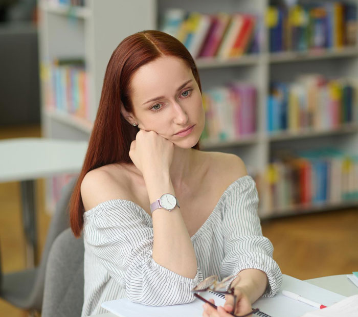 Young woman looking concerned and thoughtful while sitting at a desk, suspecting inappropriate intentions from colleague. Young woman looking concerned and thoughtful while sitting at a desk, suspecting inappropriate intentions from colleague.