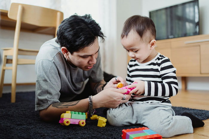 Teen caring for a young child playing with colorful toys on the floor in a bright home setting.