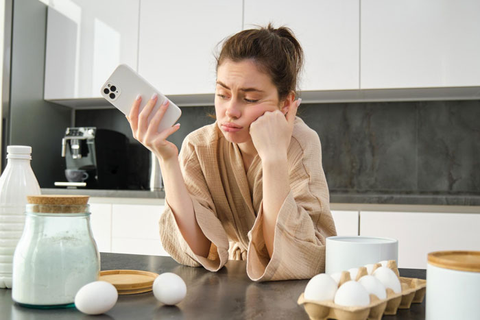 Woman cancels Thanksgiving, frustrated in kitchen holding phone amid eggs and baking supplies