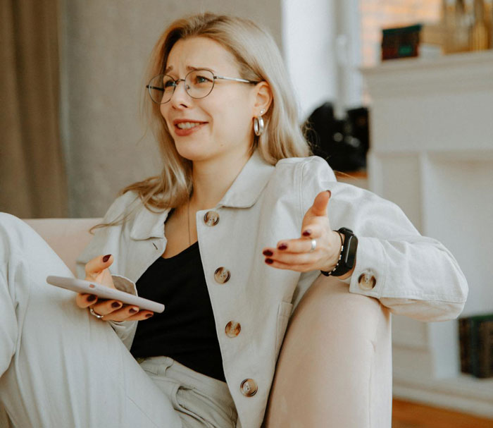 Woman with glasses and beige outfit holding phone, discussing picky eater demanding family change entire Christmas menu.