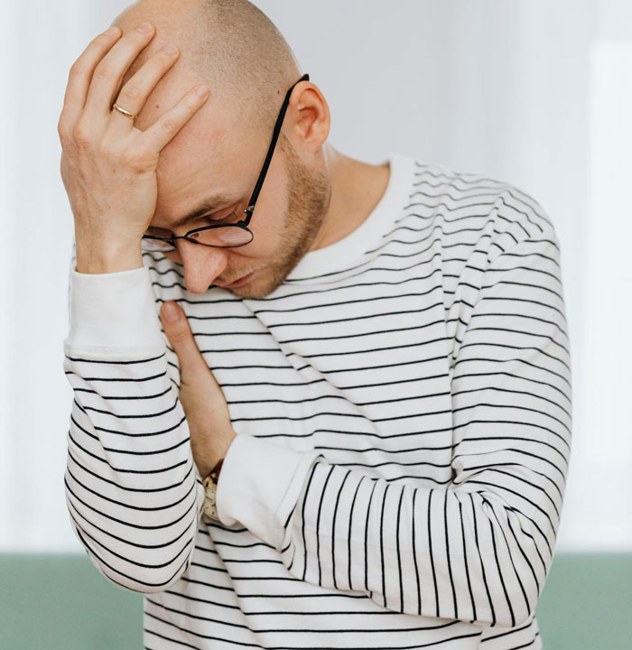 Man in striped shirt and glasses looking stressed while holding his head, illustrating picky eater dilemma at Christmas dinner.