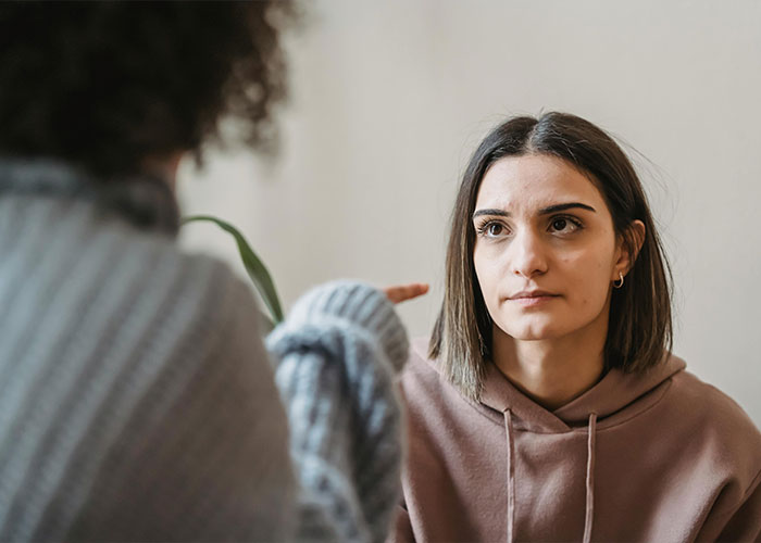 Two women having a serious conversation indoors, illustrating discomfort related to bride and groom and hairy armpits conflict.