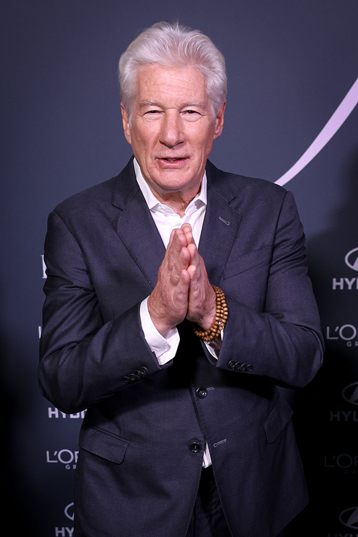 Richard Gere in a dark suit with hands together, attending a formal event related to Oscars news.