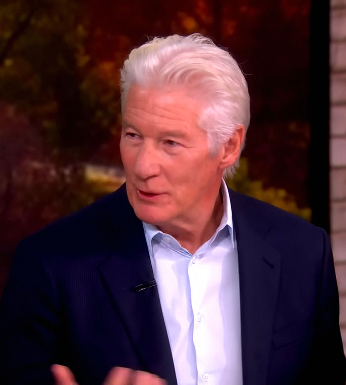 Richard Gere speaking in an interview, wearing a dark blazer and light blue shirt, discussing Oscars ban controversy.