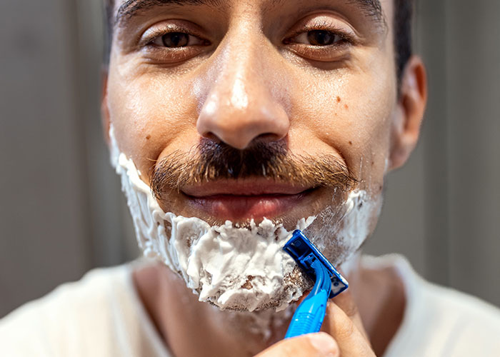 Close-up of a man shaving his face with a razor, highlighting online debates about the no makeup look preference.