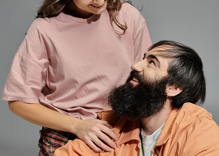 A woman smiling while looking down at a bearded man, highlighting women online roast men who prefer no makeup look.