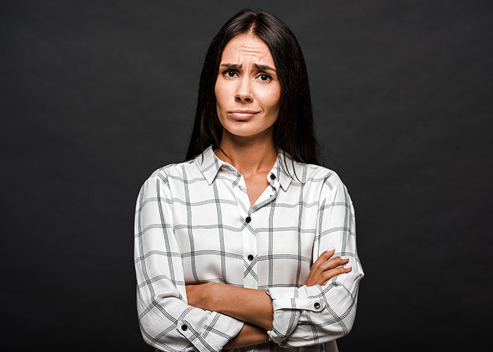 Woman with long dark hair and folded arms, showing skeptical expression, illustrating women online roasting men.
