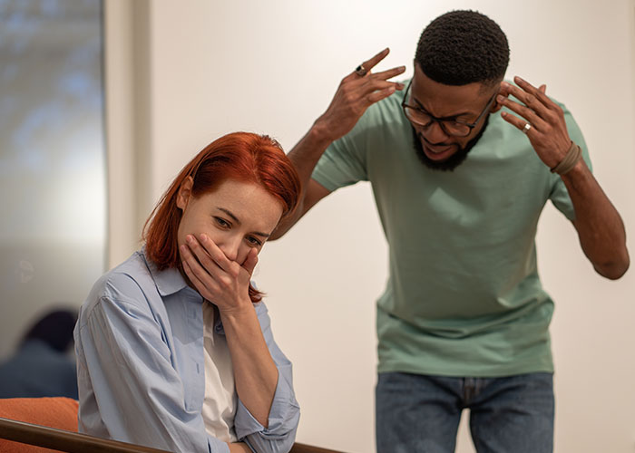 Woman covering her mouth while man angrily gestures, illustrating women online roast men preferring no makeup look debates.
