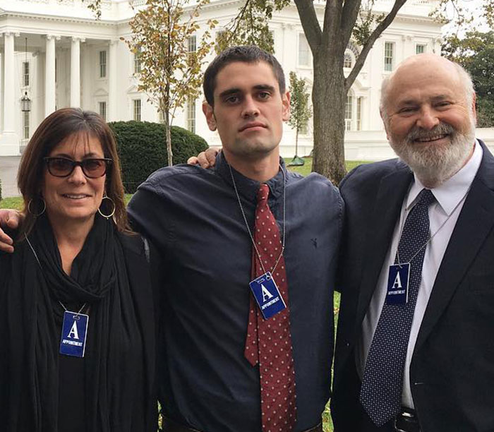 Rob Reiner’s children Jake and Romy posing outdoors with an older man near a white building, wearing appointment badges. Rob Reiner’s children Jake and Romy posing outdoors with an older man near a white building, wearing appointment badges.