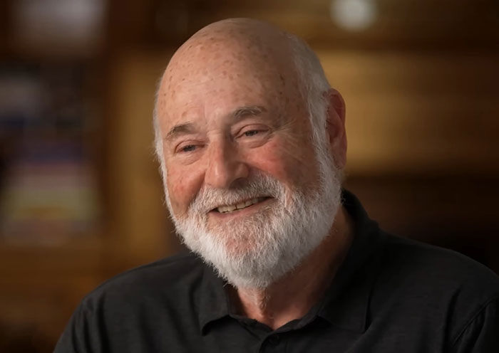 Elderly man with white beard smiling warmly in a wood-paneled room, related to person of interest after grisly LA home incident