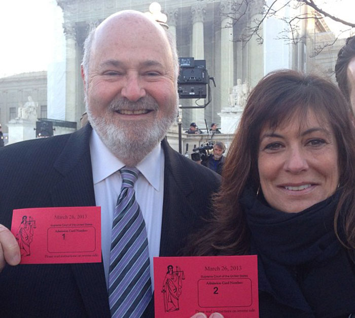 Man and woman smiling outdoors, man holding red card, related to Rob Reiner and Billy Crystal crime scene visit. Man and woman smiling outdoors, man holding red card, related to Rob Reiner and Billy Crystal crime scene visit.
