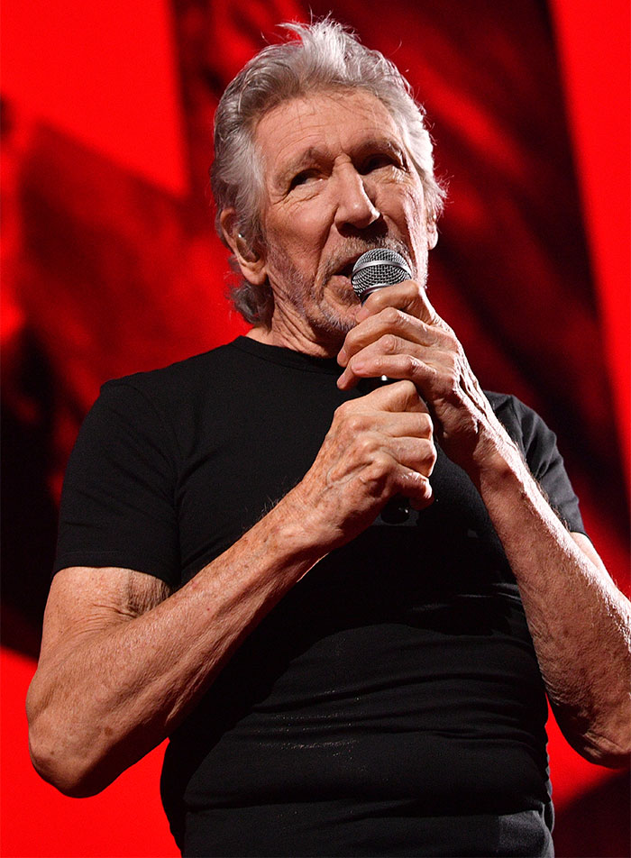 Older male singer in black shirt speaking into microphone against a red background, related to Sharon Osbourne weight loss topic Older male singer in black shirt speaking into microphone against a red background, related to Sharon Osbourne weight loss topic